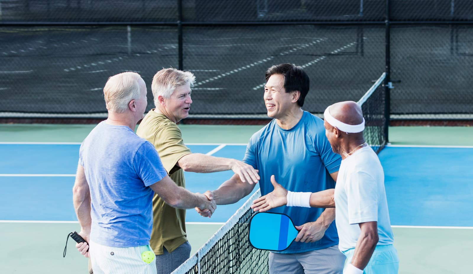 Friends shaking hands over a pickeball net.